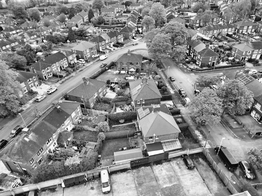 A quiet residential street featuring modern terraced homes with varying brick facades, some painted white, and pitched roofs with slate tiles. The front gardens are neatly maintained, separated by wel